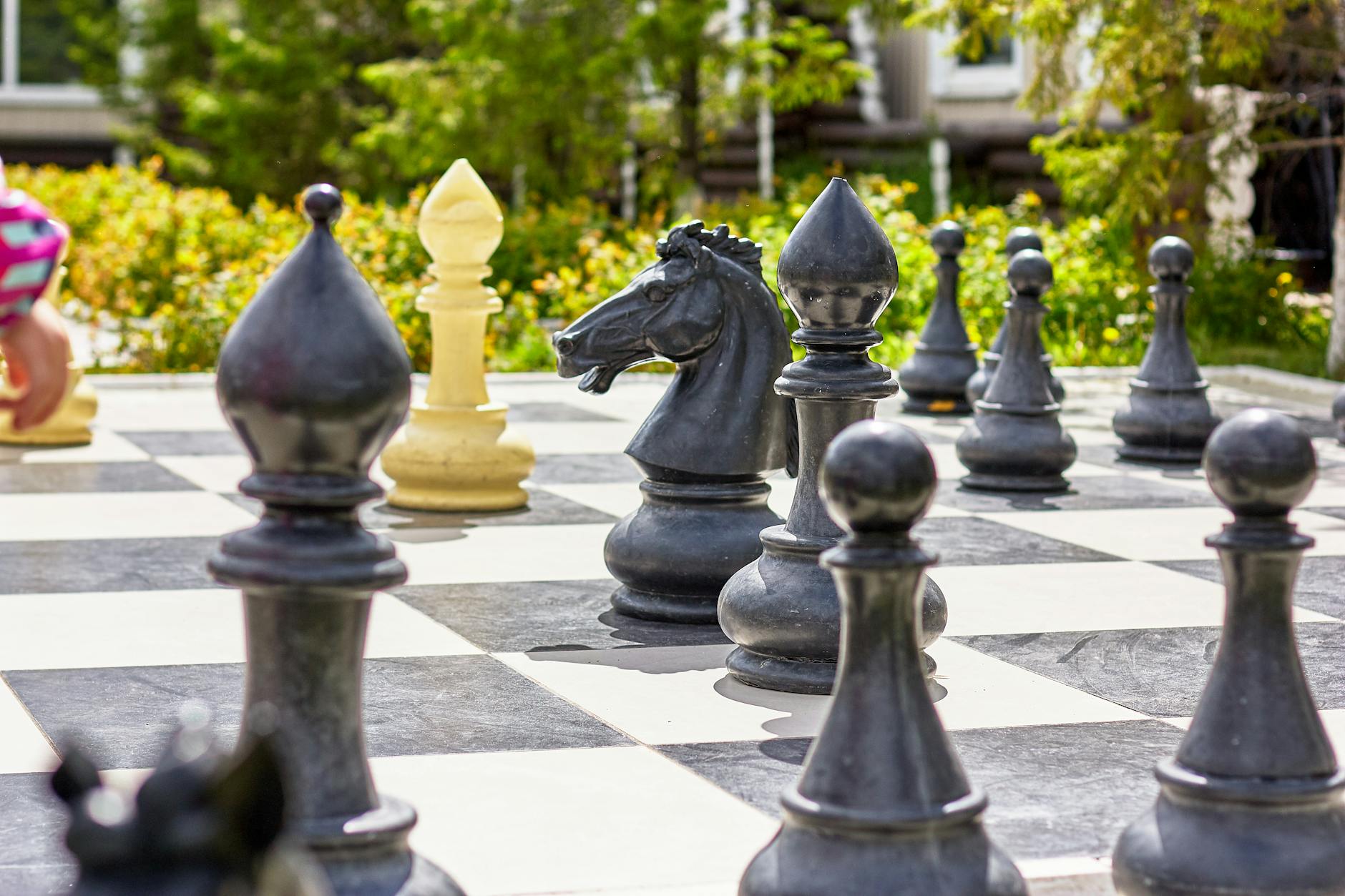 Giant chess set with figures and checkered board placed on ground in garden on sunny day