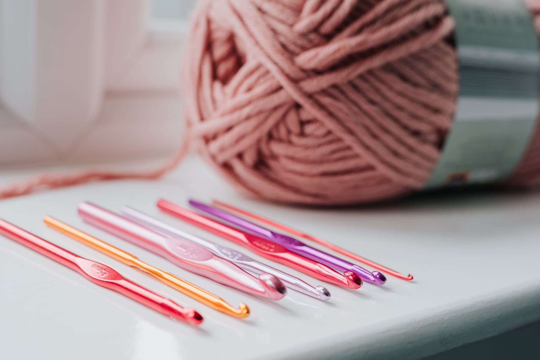 Closeup of row of multicolored crochet needles and ball of beige threads for knitting in bright room