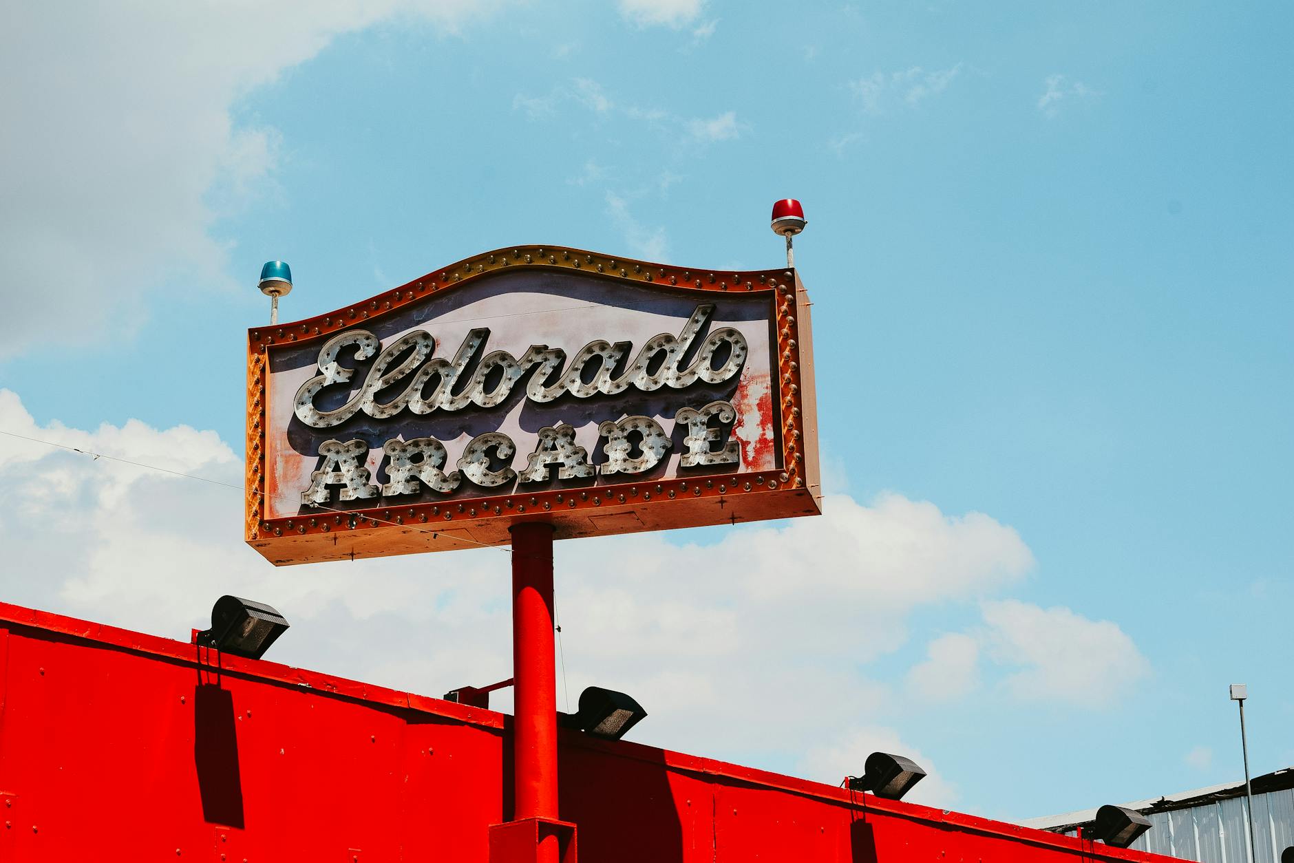 From below of signboard promoting arcade above building with red roof in sunny day