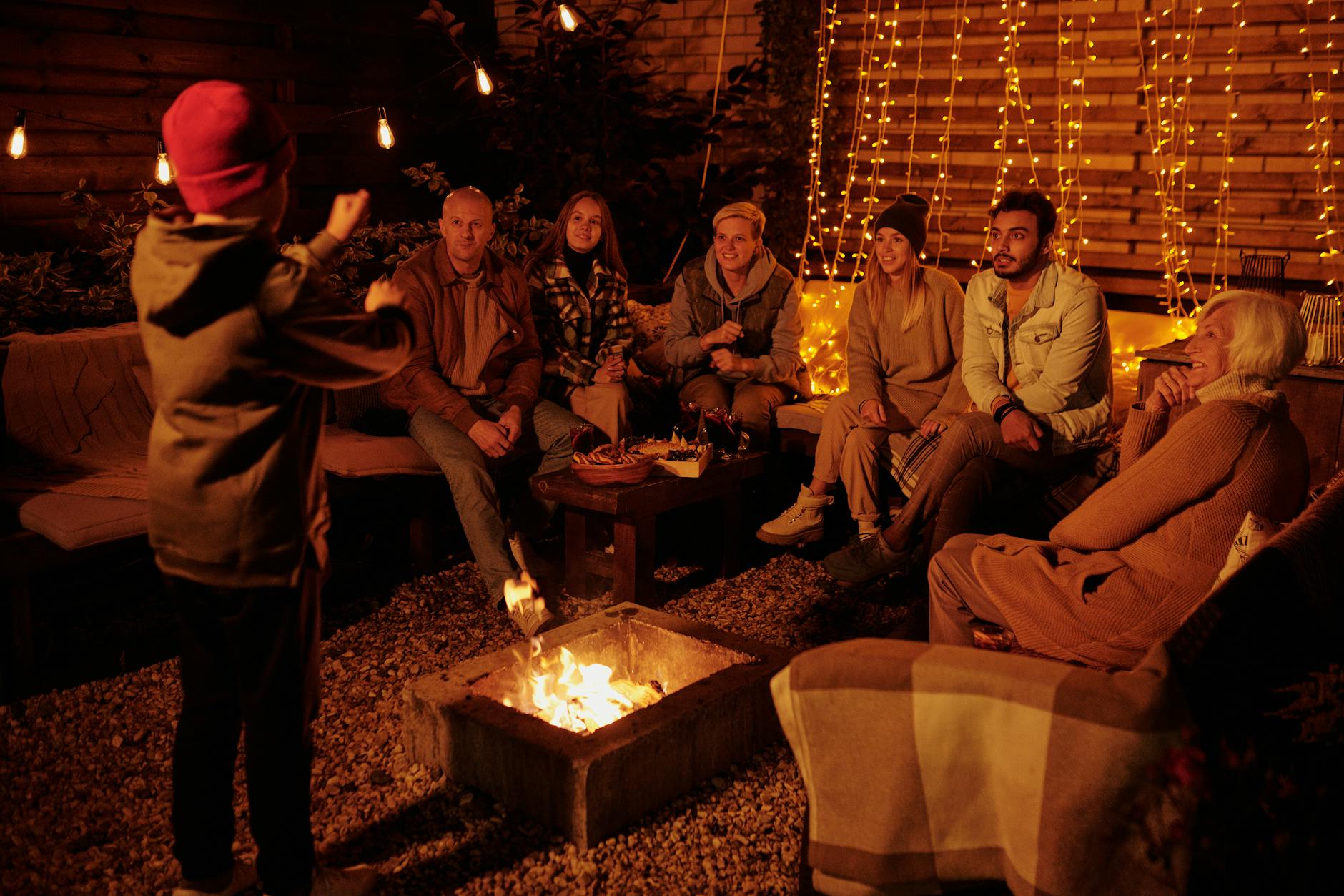 Boy acting out charade word while playing with friends and family around backyard bonfire at night