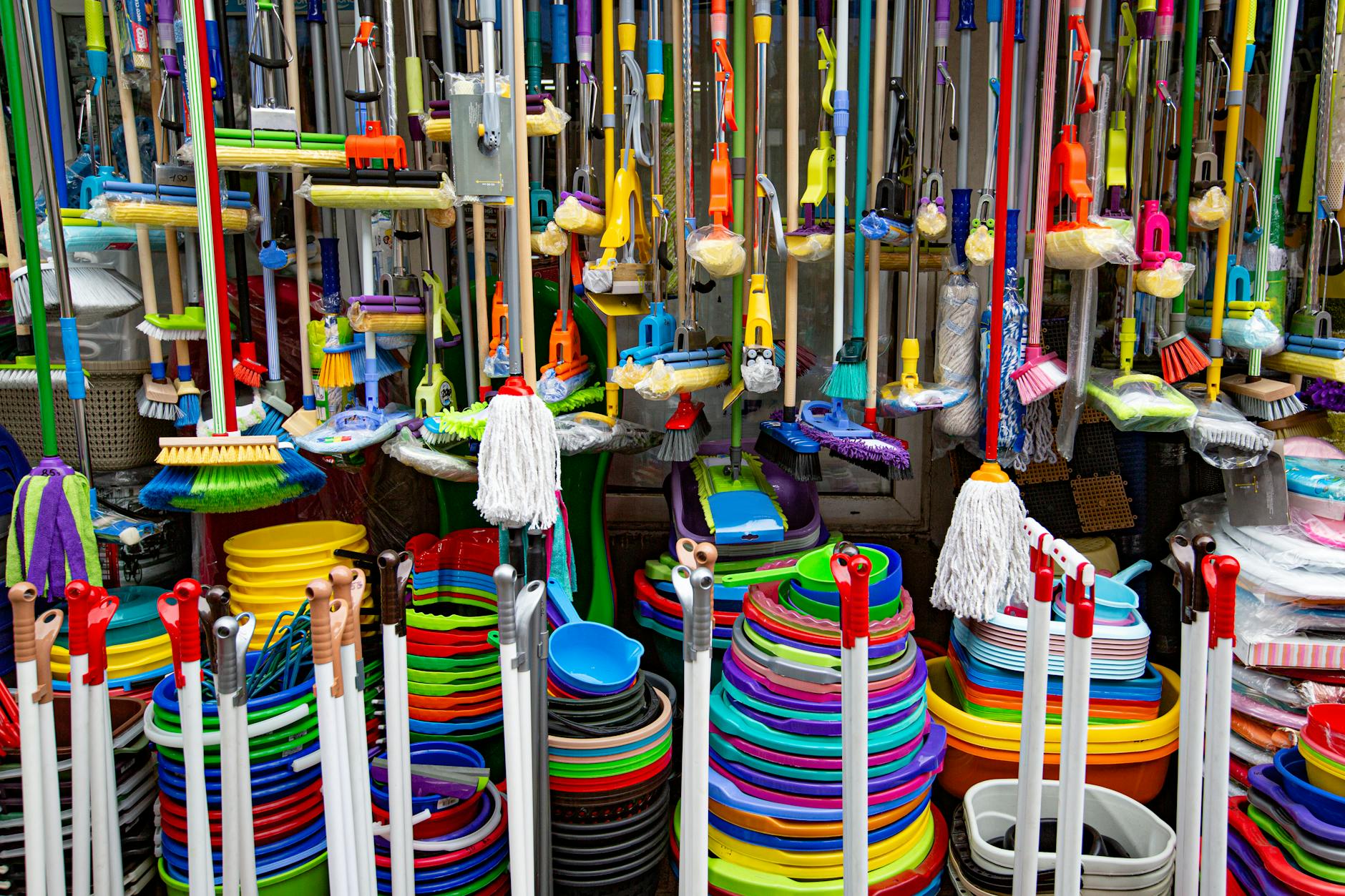 Various colorful mops and brushes arranged with stack of plastic basins and bins in household goods supermarket