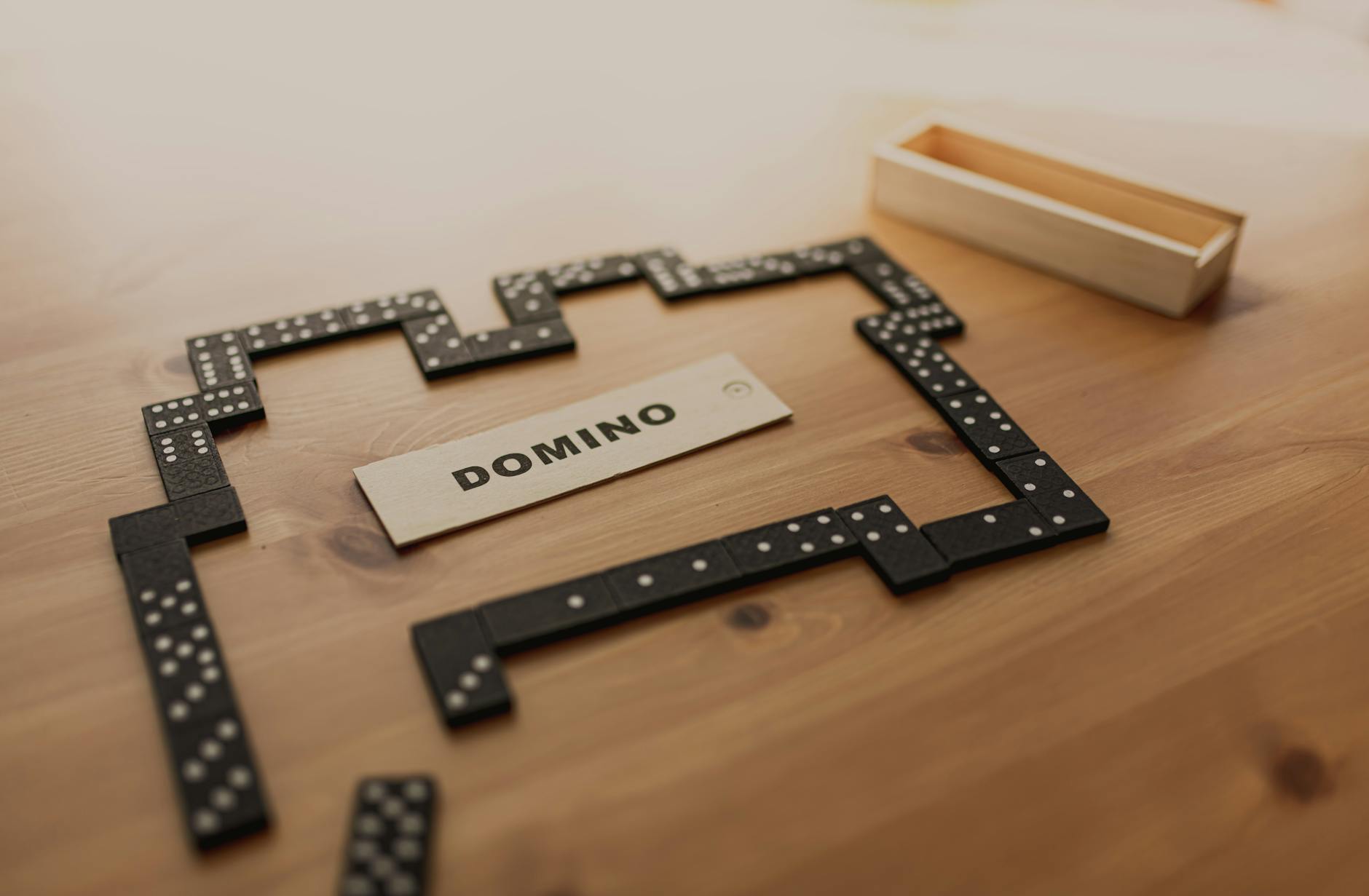 Arrangements of small black dominoes with white dots on surface and wooden box on table in sunlight