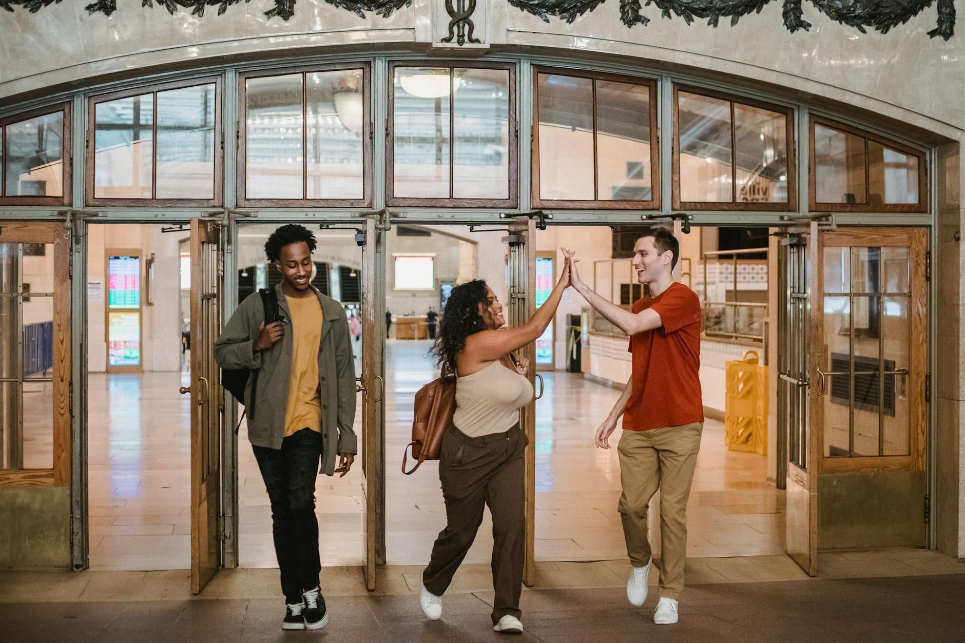 Positive diverse friends giving high five while coming out light hallway