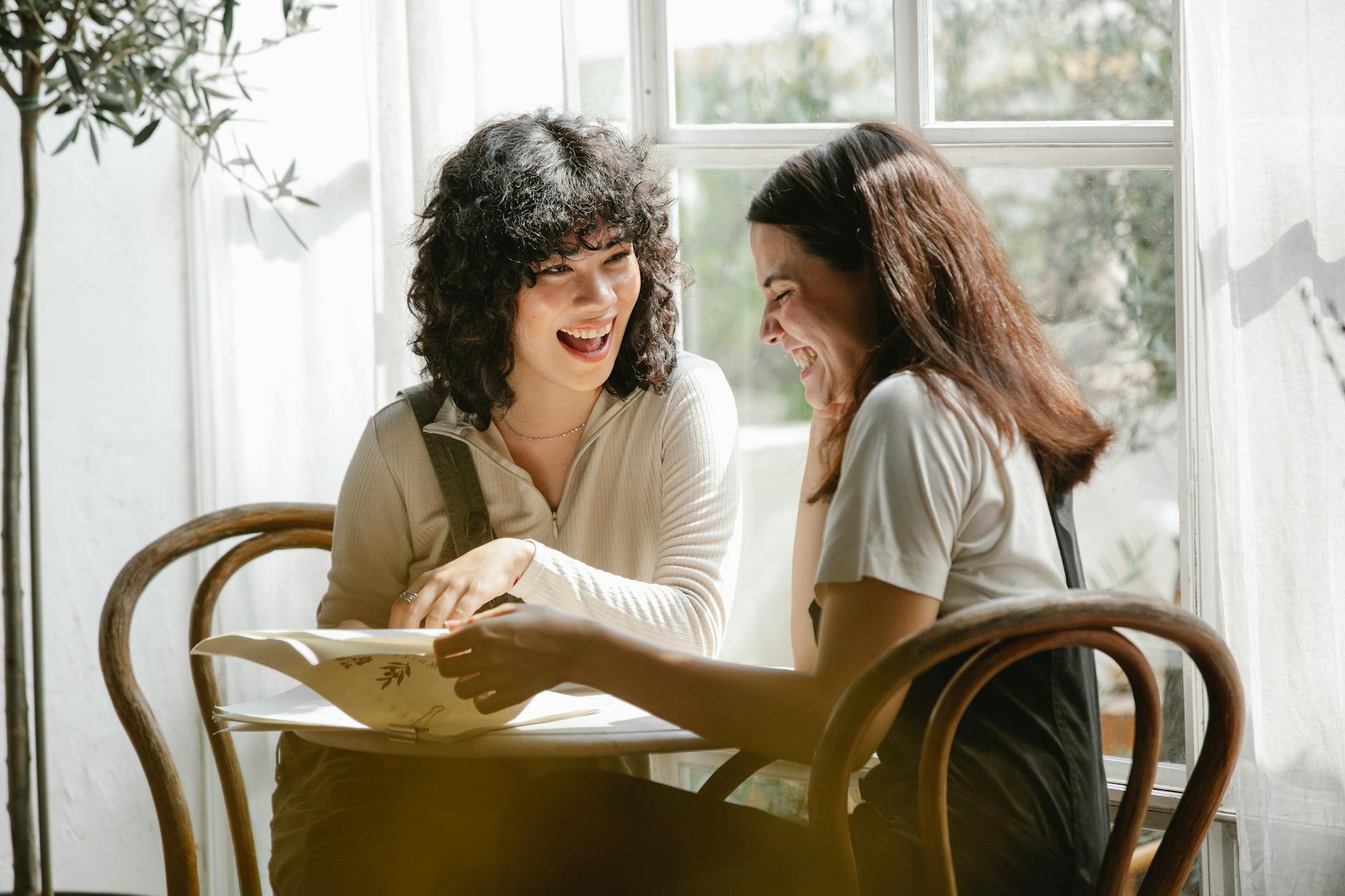 Laughing multiracial female colleagues wearing uniform flipping pages of papers while discussing work together